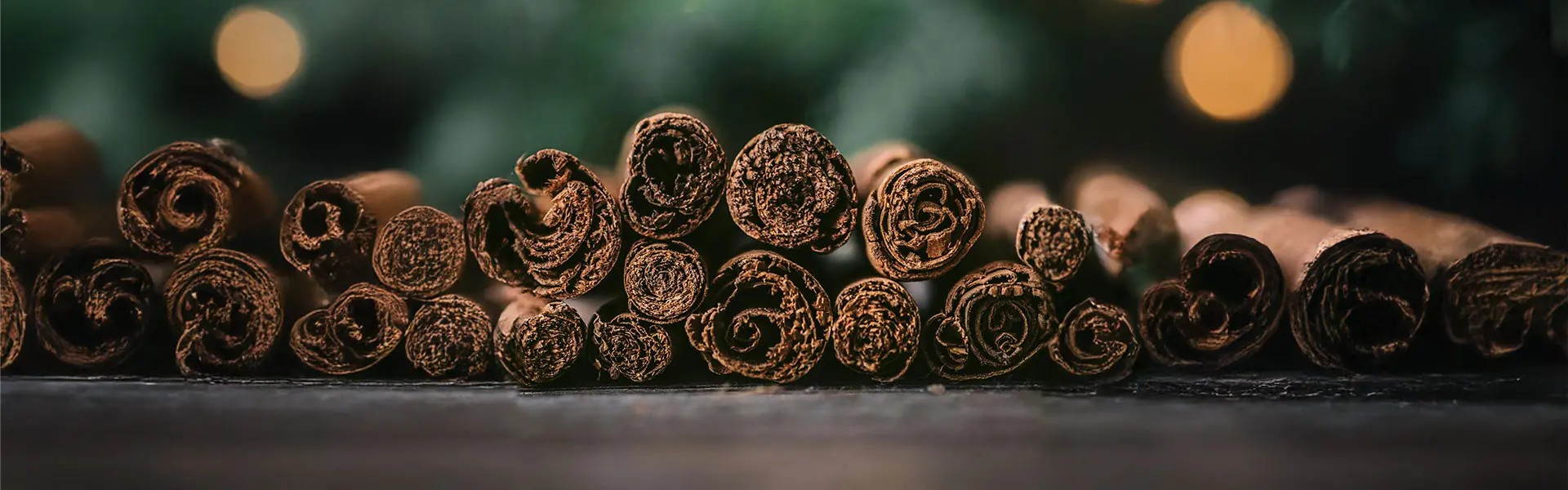 Close-up of curled ceylon cinnamon sticks stacked in a row, showcasing their rich brown hues and textured surfaces. The background is softly blurred, enhancing the warm, inviting mood.